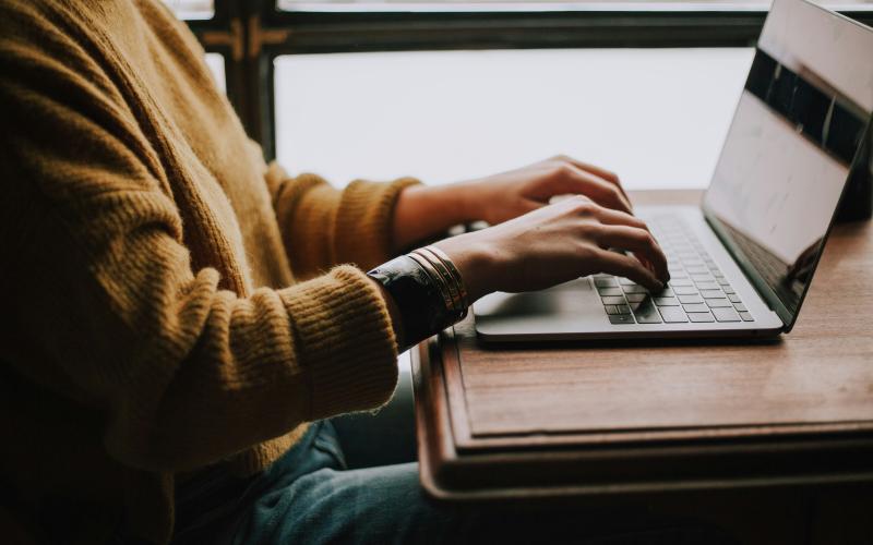 Person typing on a laptop at a wooden desk.