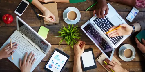 Teamwork around a table with laptops, tablets, and coffee cups.